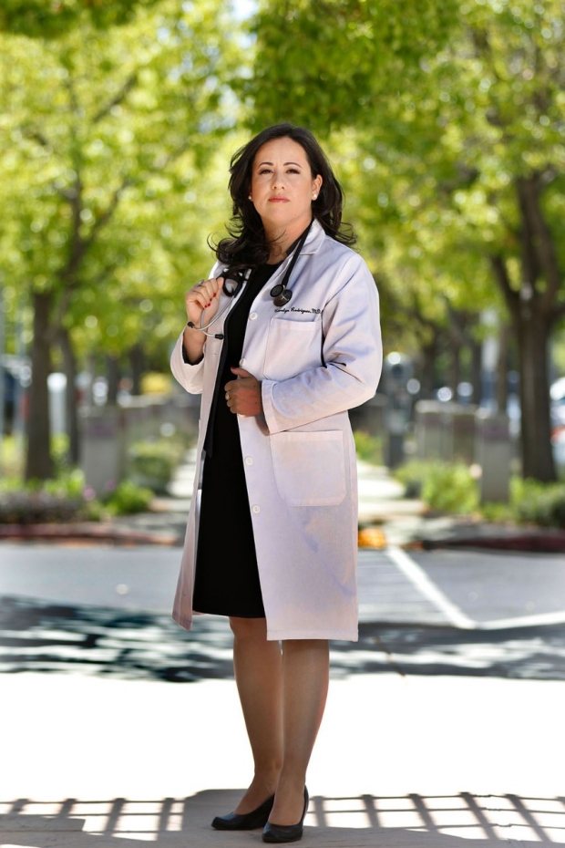Woman in a white lab coat standing on a sidewalk in front of trees