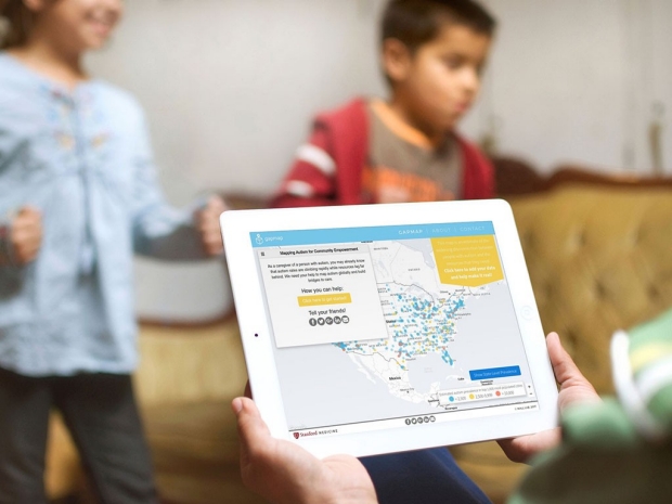 Hands holding up a tablet screen containing an autism map while two children play in the background