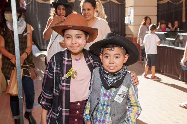 Young girl with her arm around a young boy, both wearing cowboy outfits