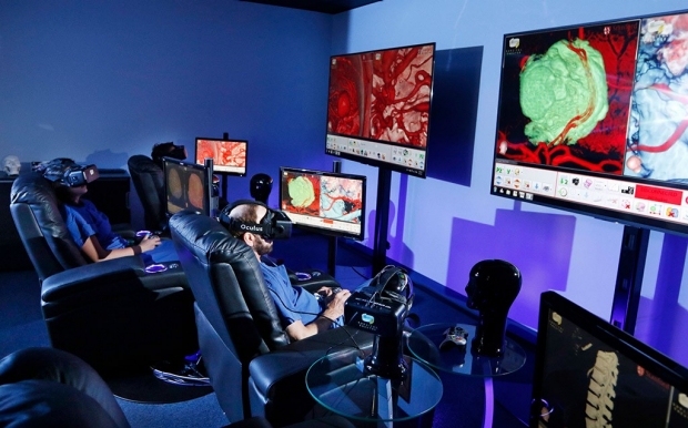Two people sitting in chairs and wearing virtual-reality headsets as the look at screens with images of a brain