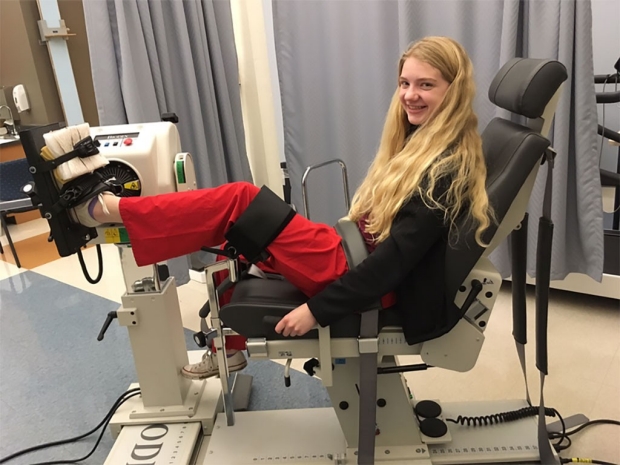 Teenage girl sitting in a machine to strengthen her left leg