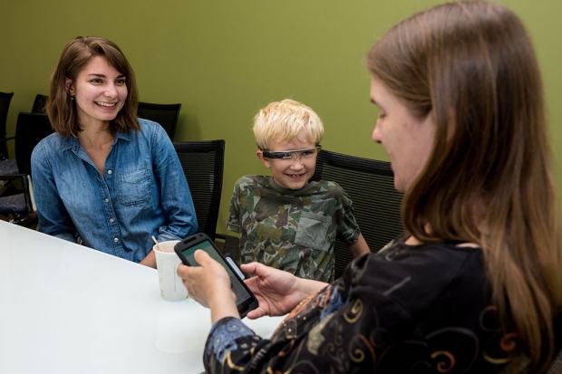Two women sit at a table with a boy wearing Google Glass